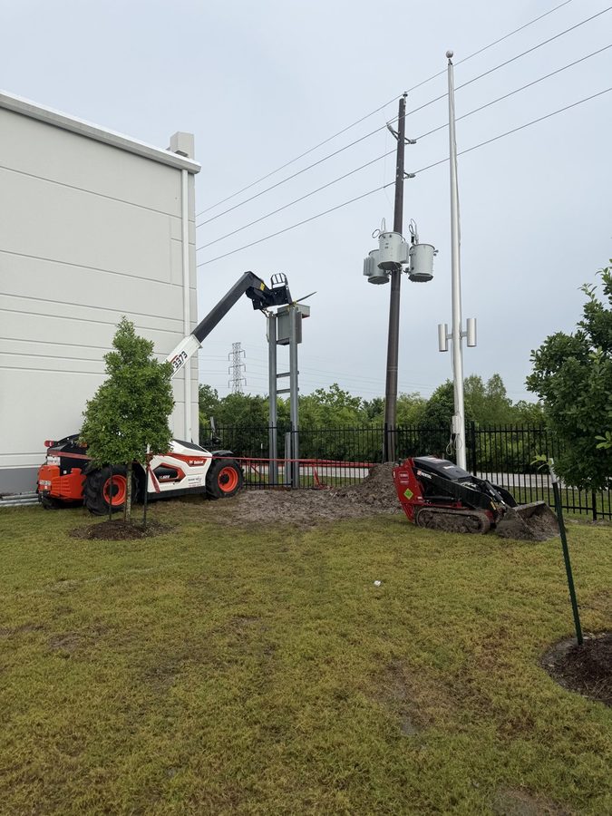 Wide view of a new riser structure with pole transformers and a telehandler on site