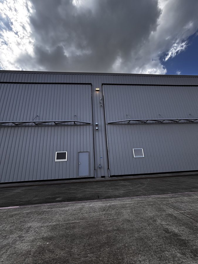 Exterior of a metal aircraft hangar with full-height sliding doors, shot under a heavy storm sky