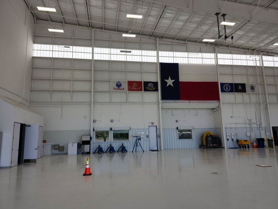 Wide interior of a finished aviation hangar with linear LED high-bay lighting, clerestory glazing and a Texas flag hung on the far wall