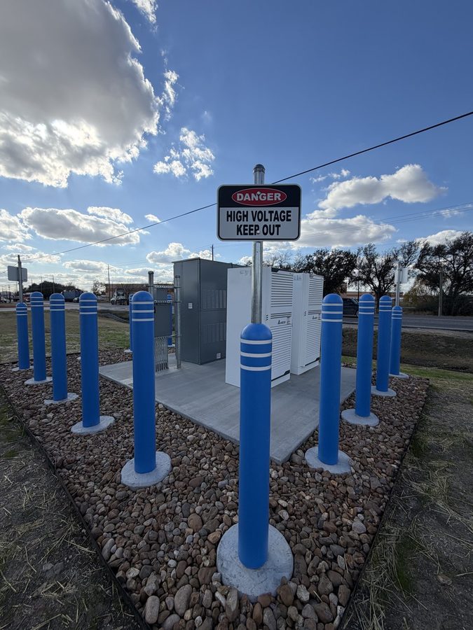 White switchgear cabinets inside a bollard-protected enclosure with high voltage warning signage