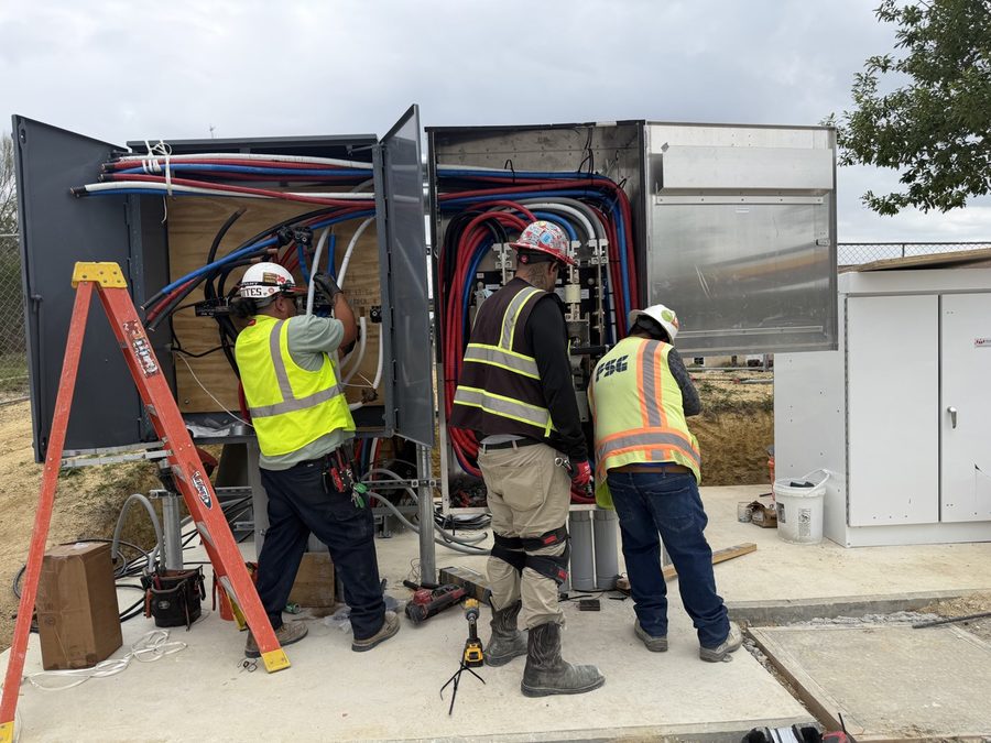 Three electricians working inside an open switchgear cabinet on red, white and blue conductors