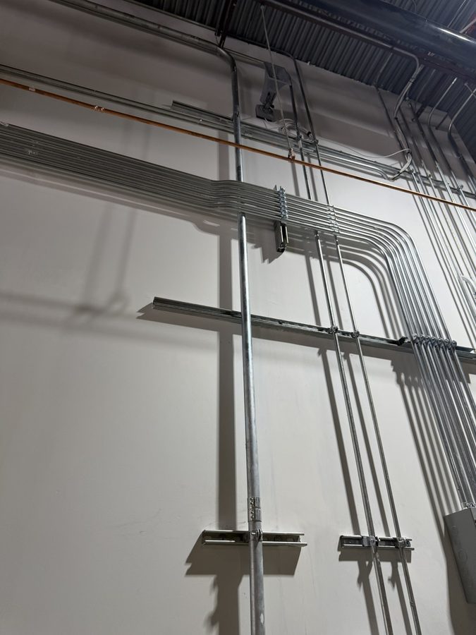 Neat EMT conduit runs with matched 90 degree bends along a warehouse wall and ceiling