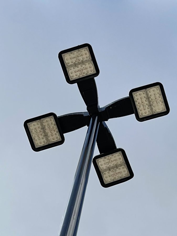 Four-head LED parking lot pole light shot from below against a clear blue sky