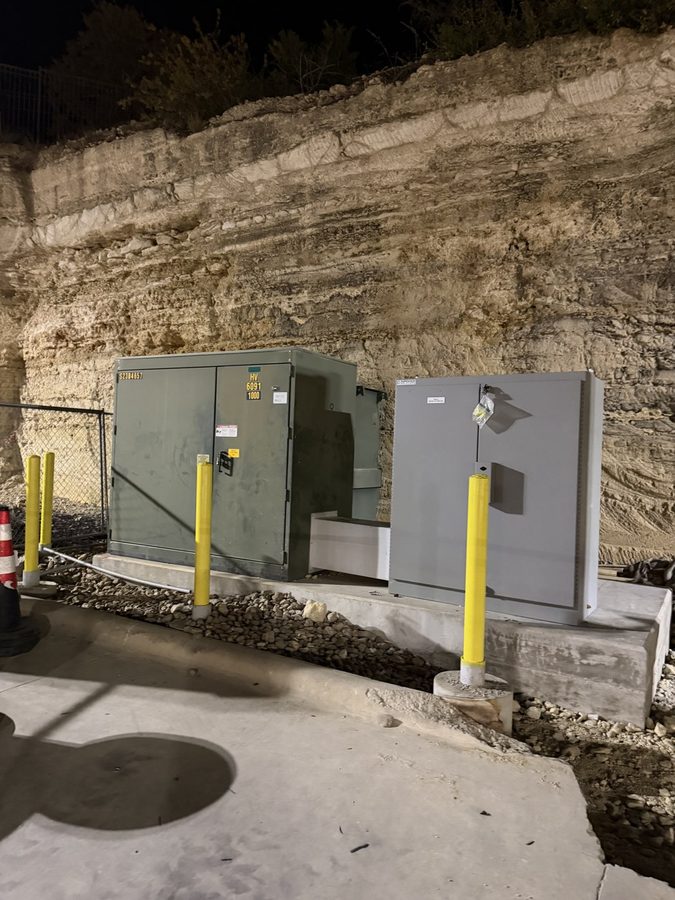 Pad-mounted transformer and disconnect cabinet lit at night behind yellow bollards