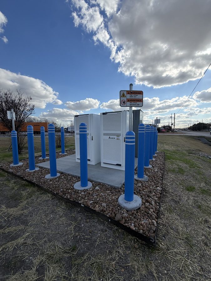 DC fast-charging power and inverter cabinets inside a ring of protective bollards