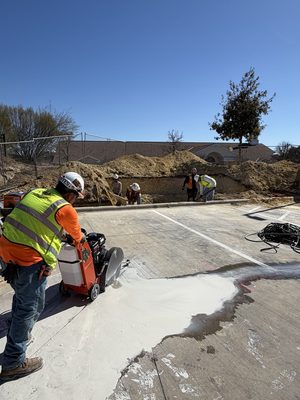 Four All American Electric crew members in hi-vis operating a walk-behind concrete saw in a parking lot