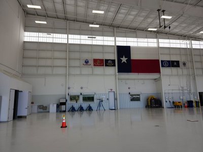 Wide interior of a finished aviation hangar with linear LED high-bay lighting, clerestory glazing and a Texas flag hung on the far wall