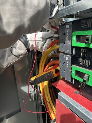 Clamp meter testing stacked molded-case breakers behind an arc-flash barrier