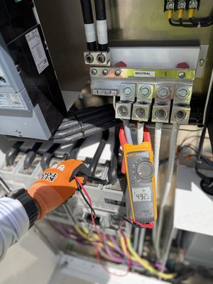Clamp meter reading voltage on a panel neutral bus bar during testing