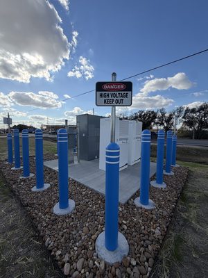 White switchgear cabinets inside a bollard-protected enclosure with high voltage warning signage
