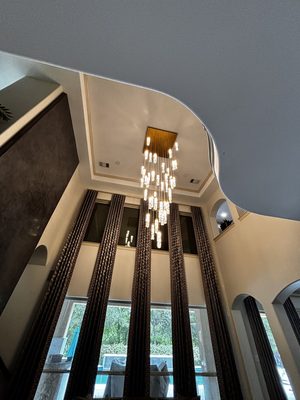 Cascading crystal and LED pendant hung in a two-story foyer with floor-to-ceiling drapery