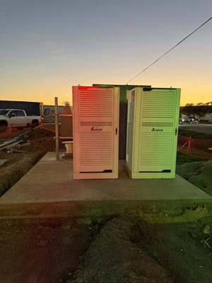 Two DC fast-charging power cabinets standing on a new concrete pad at dusk