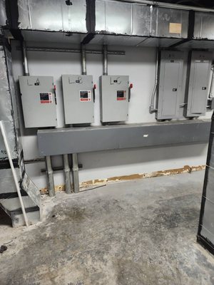 Three labeled fusible safety switches mounted in a row above a wireway in an interior electrical room, with conduit drops to each