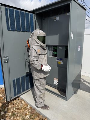 Technician in full arc-flash PPE working at an open electrical panel