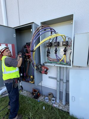 Electrician in hi-vis landing color-coded conductors into three 200-amp meter sockets on a CT cabinet