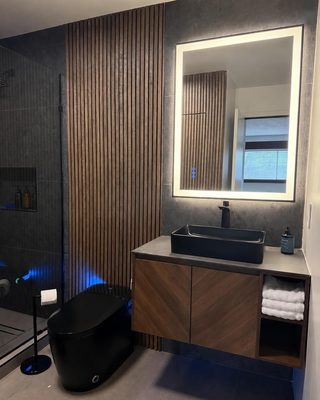 Finished bathroom with a backlit LED mirror, accent lighting and a wood slat wall