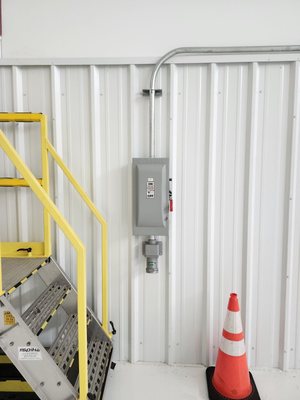 Safety disconnect and conduit run on the white interior wall of a hangar, beside a rolling work stair