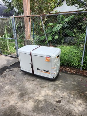 Generac home standby generator delivered onto its concrete pad in a fenced back yard, still strapped
