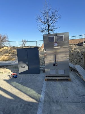 Stainless switchgear and transfer switch enclosure with a gray panel on a concrete pad