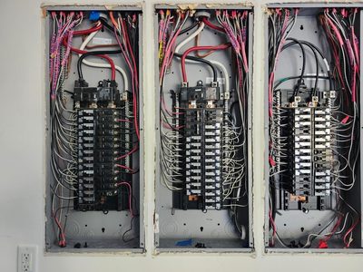 Three load centers open side by side on one wall, breakers landed and every branch circuit tagged at the top of the can