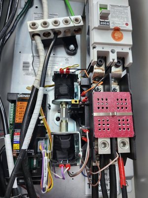 Inside an automatic transfer switch: the 200-amp main breaker, the lug bar, the transfer contactor and the red perforated terminal guard