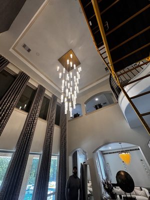 Chandelier lit in a tall foyer with the pool visible through the window behind