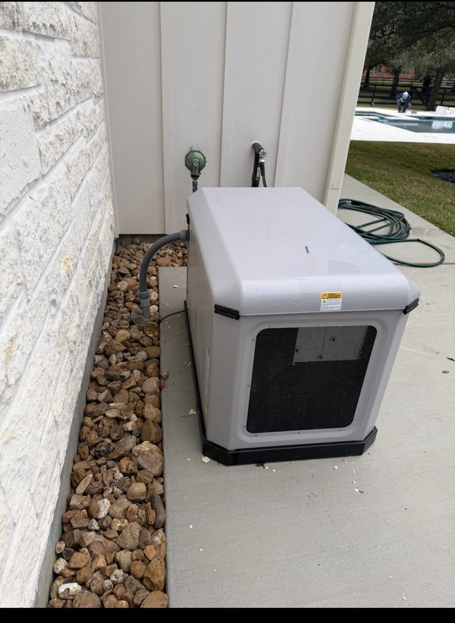 Finished home standby generator installed on its pad against the brick side wall of a Houston house
