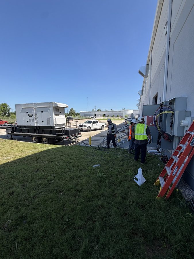 Trailer-mounted generator parked beside a commercial building as a three-man crew walks to the service entrance