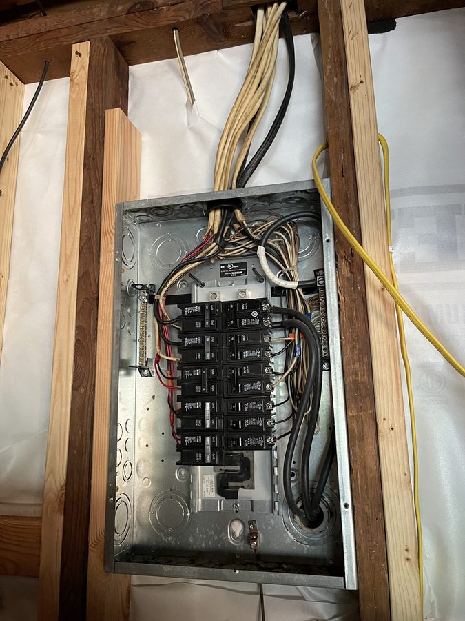 New electrical panel set in open stud framing with the breakers landed before drywall