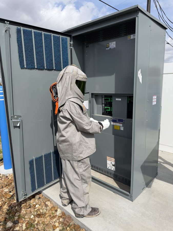 Licensed electrician in arc-flash PPE standing at an open panel ready to test